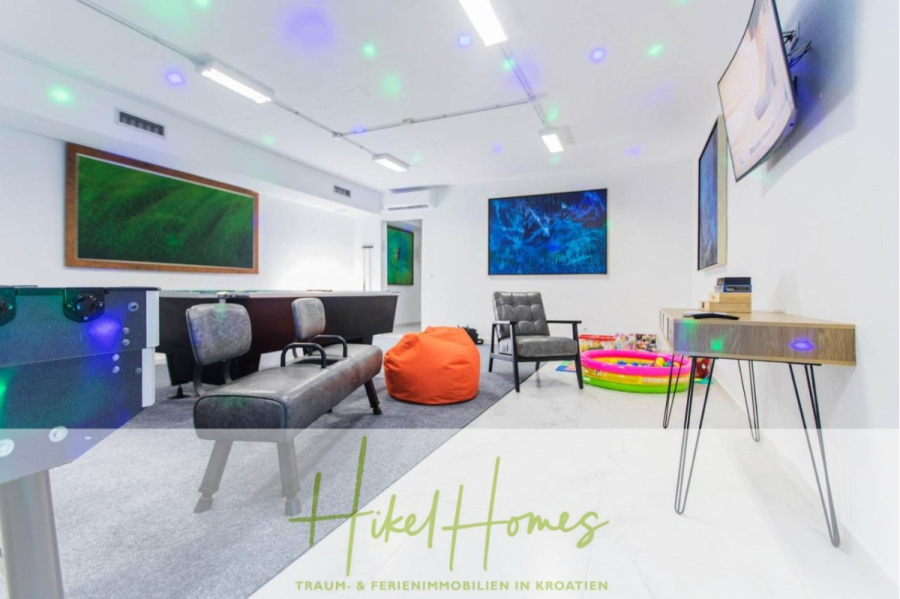 Meerblick auf 2903m² großem Grundstück in wunderbarer Alleinlage am Stadtrand von Split - Ein modernes Spielzimmer mit Sofas, Loungesesseln, einem Sitzsack, einem Billardtisch, Wandkunst und einem Fernseher. In der Ecke befindet sich ein Spielbereich für Kinder mit einem kleinen aufblasbaren Pool. "Hikel Homes" steht quer über das Bild geschrieben. (45855)