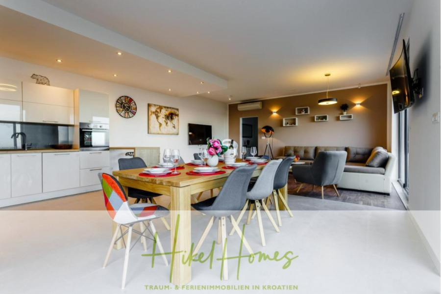 Meerblick auf 2903m² großem Grundstück in wunderbarer Alleinlage am Stadtrand von Split - Moderne offene Küche und Wohnzimmer mit einem Esstisch aus Holz für vier Personen, bunten Stühlen, einem hellgrauen Sofa, Wandkunst und Regalen. Der Raum ist hell, stilvoll und ordentlich eingerichtet. (45849)