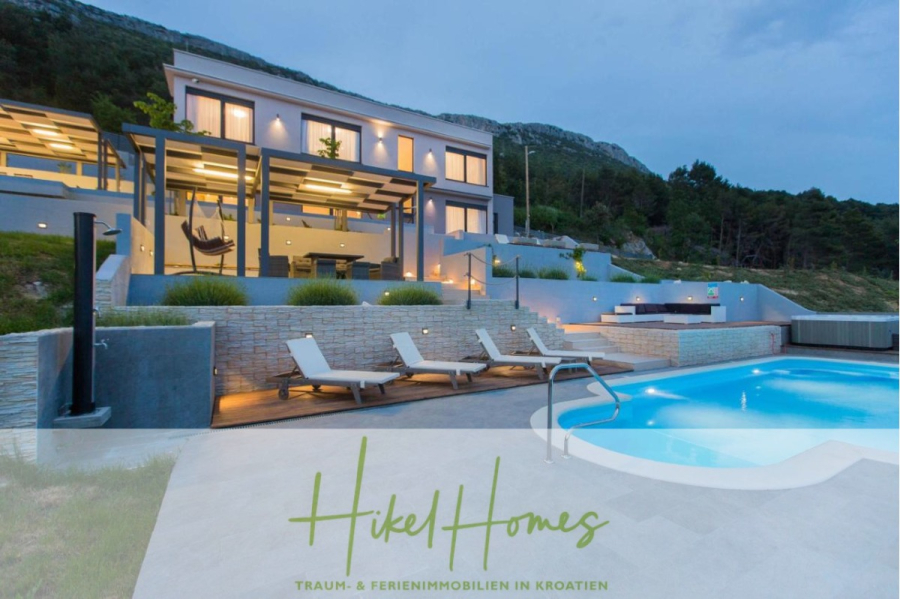 Meerblick auf 2903m² großem Grundstück in wunderbarer Alleinlage am Stadtrand von Split - Moderne Villa mit großen Fenstern, Terrassen, Sitzgelegenheiten im Freien, einem Swimmingpool und Blick auf die Hügel in der Abenddämmerung. "Hikel Homes: Traum- & Ferienimmobilien in Kroatien" ist am unteren Rand des Bildes zu lesen. (45861)