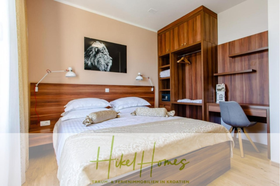 Meerblick auf 2903m² großem Grundstück in wunderbarer Alleinlage am Stadtrand von Split - Ein modernes Hotelzimmer mit einem Doppelbett, einem Kopfteil aus Holz, an der Wand angebrachten Leselampen, einem offenen Kleiderschrank, einem Schreibtisch mit Stuhl und einem Schwarz-Weiß-Löwenbild über dem Bett. Helle Wände und Bettzeug schaffen eine helle Atmosphäre. (45846)