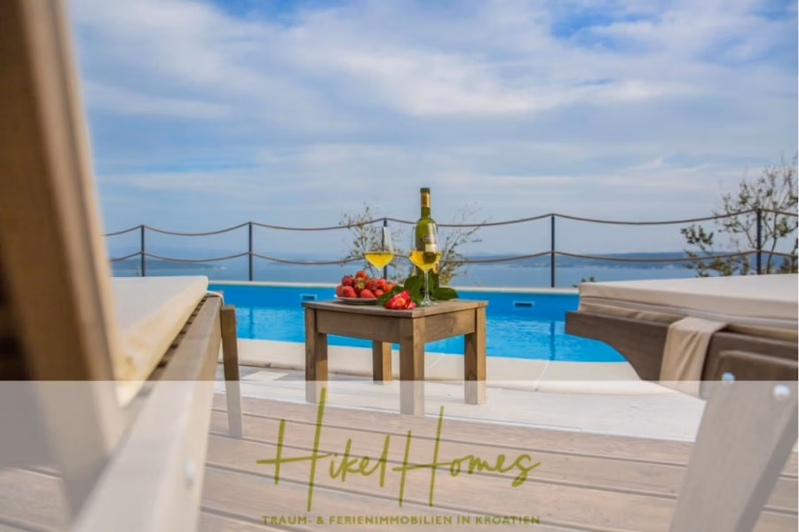 Meerblick auf 2903m² großem Grundstück in wunderbarer Alleinlage am Stadtrand von Split - Blick auf eine Poolszene mit einem Holztisch, auf dem eine Weinflasche, zwei gefüllte Gläser und Erdbeeren stehen. Liegestühle rahmen die Szene ein, und unter blauem Himmel ist ein Blick auf das Meer in der Ferne zu sehen. (41454)