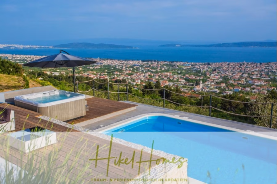 Meerblick auf 2903m² großem Grundstück in wunderbarer Alleinlage am Stadtrand von Split - Luxuriöser Außenpool und Whirlpool mit Blick auf eine malerische Küstenstadt in Kroatien. Ein schwarzer Sonnenschirm spendet Schatten auf der Holzterrasse. Die Landschaft besticht durch üppiges Grün und eine weite, blaue Meeresfläche unter klarem Himmel. (41456)