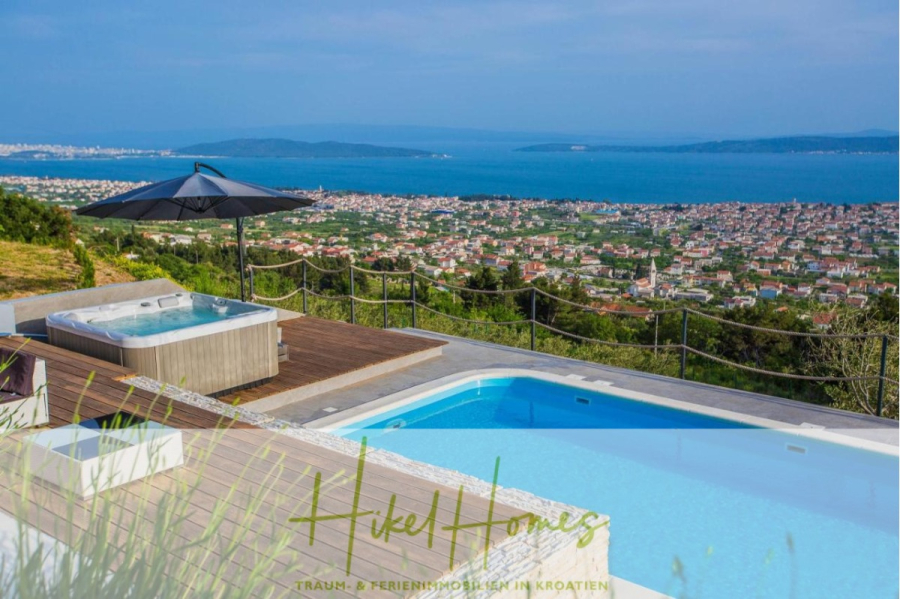 Meerblick auf 2903m² großem Grundstück in wunderbarer Alleinlage am Stadtrand von Split - Infinity-Pool und Whirlpool auf einem Holzdeck mit Blick auf eine Küstenstadt und das Meer, mit Hügeln, blauem Himmel und einem großen Sonnenschirm als Schattenspender. Üppiges Grün umgibt den modernen Außenbereich. (45874)