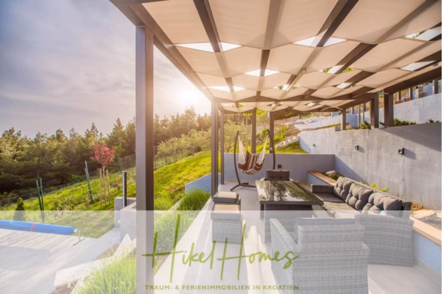 Meerblick auf 2903m² großem Grundstück in wunderbarer Alleinlage am Stadtrand von Split - Außenterrasse mit modernen Möbeln, Hängematte und schattiger Pergola. Von hier aus hat man einen herrlichen Blick auf die grüne Landschaft und den Sonnenuntergang. Das Design ist ruhig und einladend. Der Text unten lautet: „Hikel Homes – Traum- & Ferienimmobilien in Kroatien.“. (41449)