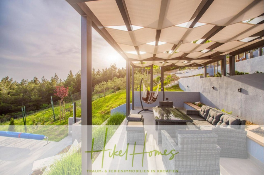 Meerblick auf 2903m² großem Grundstück in wunderbarer Alleinlage am Stadtrand von Split - Moderne Außenterrasse mit Korbmöbeln, Hängematten und einer Pergola an einem Hang mit Blick ins Grüne; das Sonnenlicht fällt durch die Pergola. Der Text "Hikel Homes Traum- & Ferienimmobilien in Kroatien" ist überlagert. (45865)