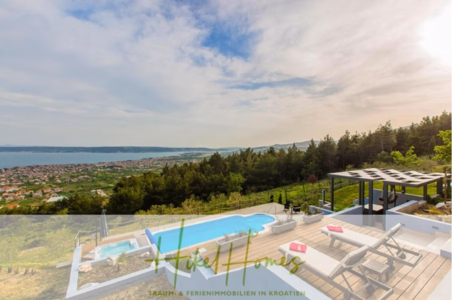 Meerblick auf 2903m² großem Grundstück in wunderbarer Alleinlage am Stadtrand von Split - Blick vom Dach einer luxuriösen Villa mit Pool auf eine üppige, grüne Landschaft und eine entfernte Küstenstadt. Der Himmel ist teilweise bewölkt, was für eine ruhige Atmosphäre sorgt. Die Terrasse verfügt über Sonnenliegen und eine Pergola. (41450)