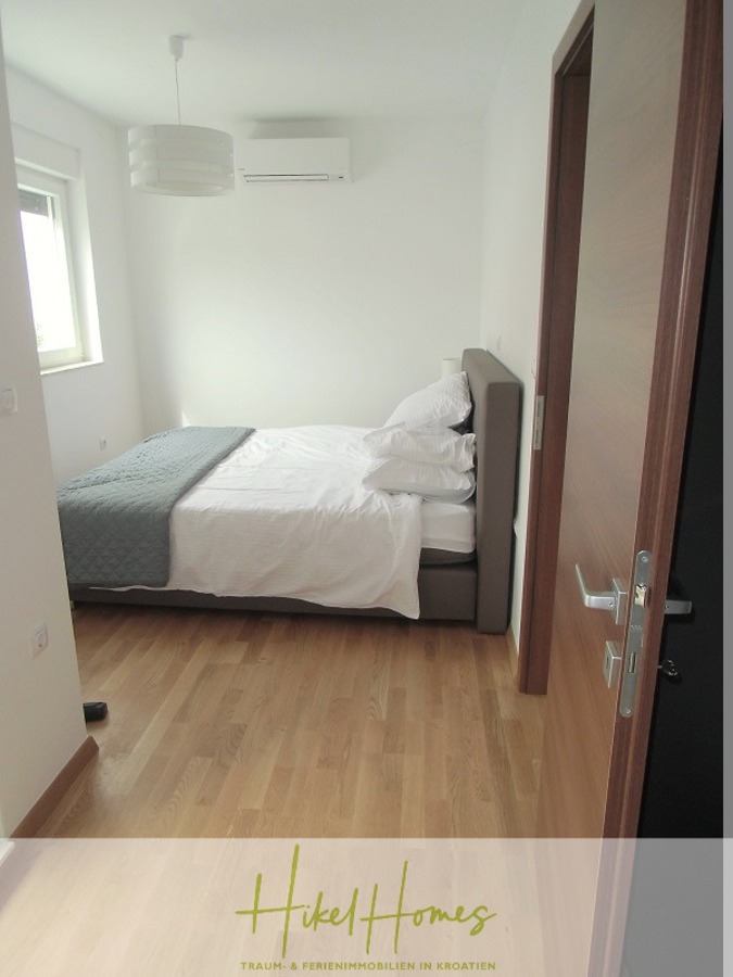 Galerie Wohnung, 3 Schlafzimmer / 70m zum Meer / Pool / 2 Bäder - Ein kleines, modernes Schlafzimmer mit Holzfußboden, einem Doppelbett mit weißer Bettwäsche und einer grauen Decke, einem Fenster, das Tageslicht hereinlässt, einer Klimaanlage über dem Bett und einer weißen Hängelampe an der Decke. (46578)