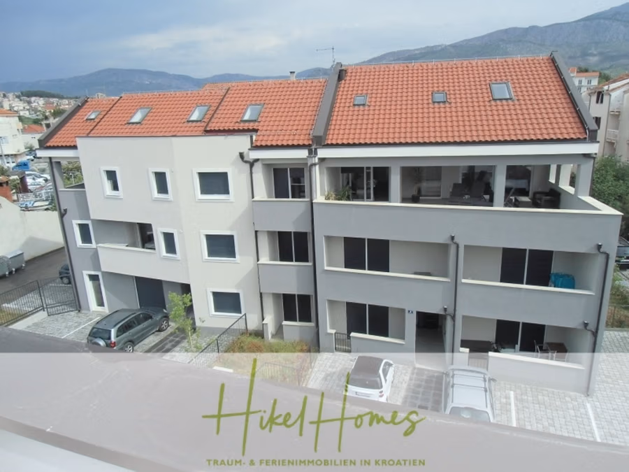 Galerie Wohnung, 3 Schlafzimmer / 70m zum Meer / Pool / 2 Bäder - Ein modernes, dreistöckiges Wohnhaus mit rotem Ziegeldach und Balkonen. Es hat mehrere Fenster und ist von einem gepflasterten Innenhof mit parkenden Autos umgeben. Im Hintergrund sind Hügel zu sehen. Unten steht der Text: „HikelHomes“. (41250)