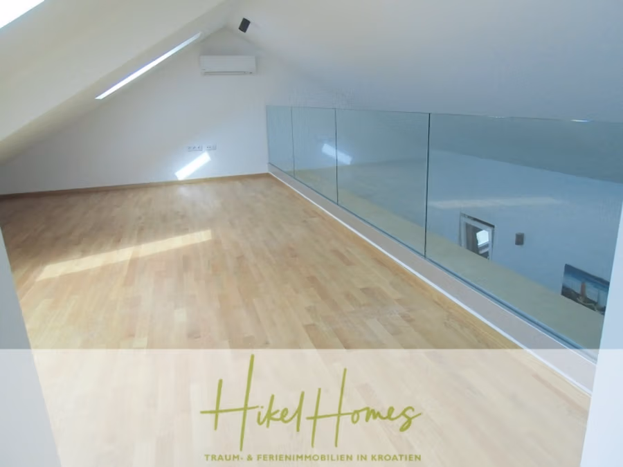 Galerie Wohnung, 3 Schlafzimmer / 70m zum Meer / Pool / 2 Bäder - Ein moderner, lichtdurchfluteter Dachboden mit hellem Holzboden und schräger Decke mit Oberlichtern. Ein Glasgeländer umschließt einen offenen Bereich. Der Raum besticht durch weiße Wände, eine Klimaanlage und minimalistisches Design. (41259)