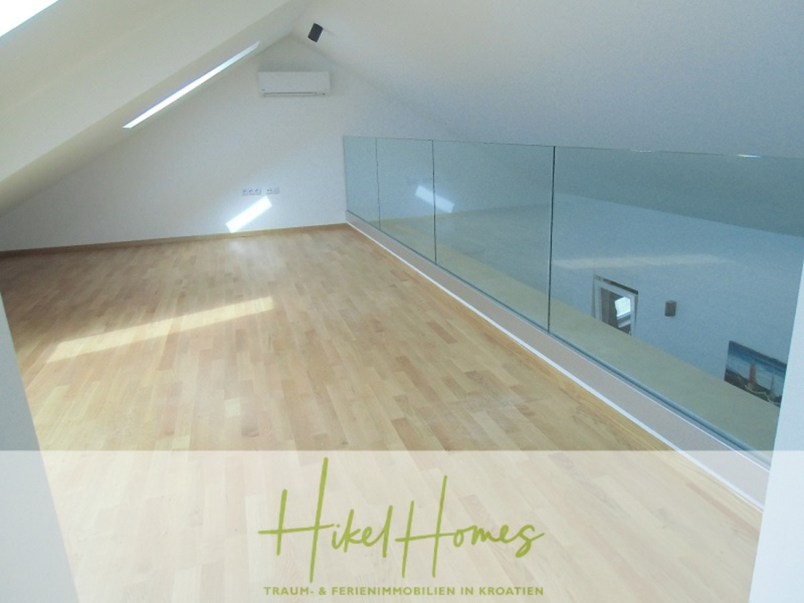 Galerie Wohnung, 3 Schlafzimmer / 70m zum Meer / Pool / 2 Bäder - Ein heller Dachraum mit schrägen Decken, Holzfußboden, einem Glasgeländer und einer kleinen Klimaanlage an der hinteren Wand. Der Raum ist leer und wird durch das natürliche Licht der Oberlichtfenster gut beleuchtet. Der Text am unteren Rand lautet "Hikel Homes. (46581)