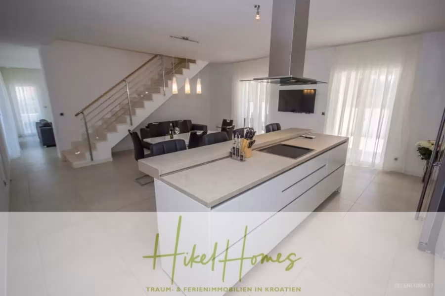 Villa im Mittelmeerstil mit 3 SZ, Pool, Dachterrasse mit Meerblick (3/4) - Moderne Küche mit eleganter Kochinsel, Barhockern und eleganter Beleuchtung. Der offene Essbereich verfügt über einen Glastisch und schwarze Stühle. Eine Treppe führt in die obere Etage. Große Fenster mit transparenten Vorhängen lassen viel Tageslicht herein. (43322)