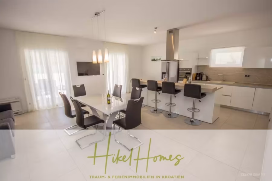 Villa im Mittelmeerstil mit 3 SZ, Pool, Dachterrasse mit Meerblick (3/4) - Moderne Küche und Essbereich mit weißem Tisch, schwarzen Stühlen und einer Kücheninsel mit Hockern. Große Fenster mit transparenten Vorhängen lassen Tageslicht herein. Der Raum ist hell und minimalistisch mit eleganten Designelementen. Die Textüberlagerung lautet: „Hikel Homes“. (43318)