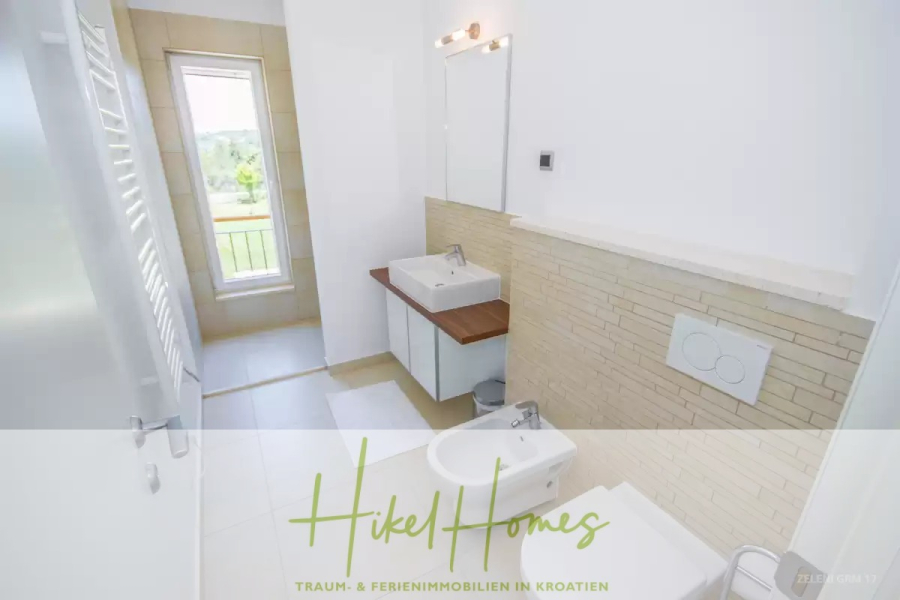 Villa im Mittelmeerstil mit 3 SZ, Pool, Dachterrasse mit Meerblick (3/4) - Helles Badezimmer mit weißen Wänden, modernem Waschbecken, Bidet und Toilette. Ein großes Fenster lässt natürliches Licht herein. "Hikel Homes" und deutscher Text erscheinen am unteren Rand des Bildes. (45766)