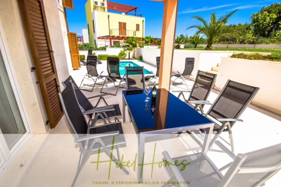 Villa im Mittelmeerstil mit 3 SZ, Pool, Dachterrasse mit Meerblick (3/4) - Moderne Außenterrasse mit schwarzen Stühlen und einem Tisch für Getränke, mit Blick auf einen kleinen Swimmingpool und Sonnenliegen. Heller, sonniger Tag mit einem gelben Haus, Palmen und grünem Gras im Hintergrund. (45748)