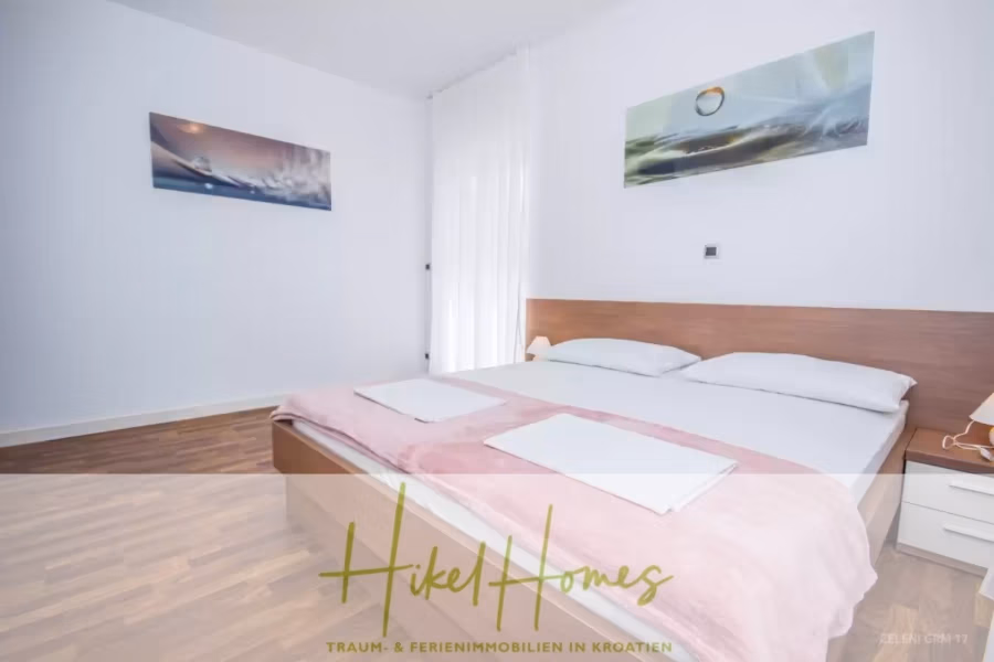 Villa im Mittelmeerstil mit 3 SZ, Pool, Dachterrasse mit Meerblick (3/4) - Ein ordentlich eingerichtetes Schlafzimmer mit Doppelbett, rosa Decke und zwei Kissen. Die minimalistische Einrichtung umfasst zwei Wandgemälde, einen Nachttisch und transparente Vorhänge, die für Tageslicht sorgen. Der Holzboden sorgt für ein helles und einladendes Raumgefühl. (43316)