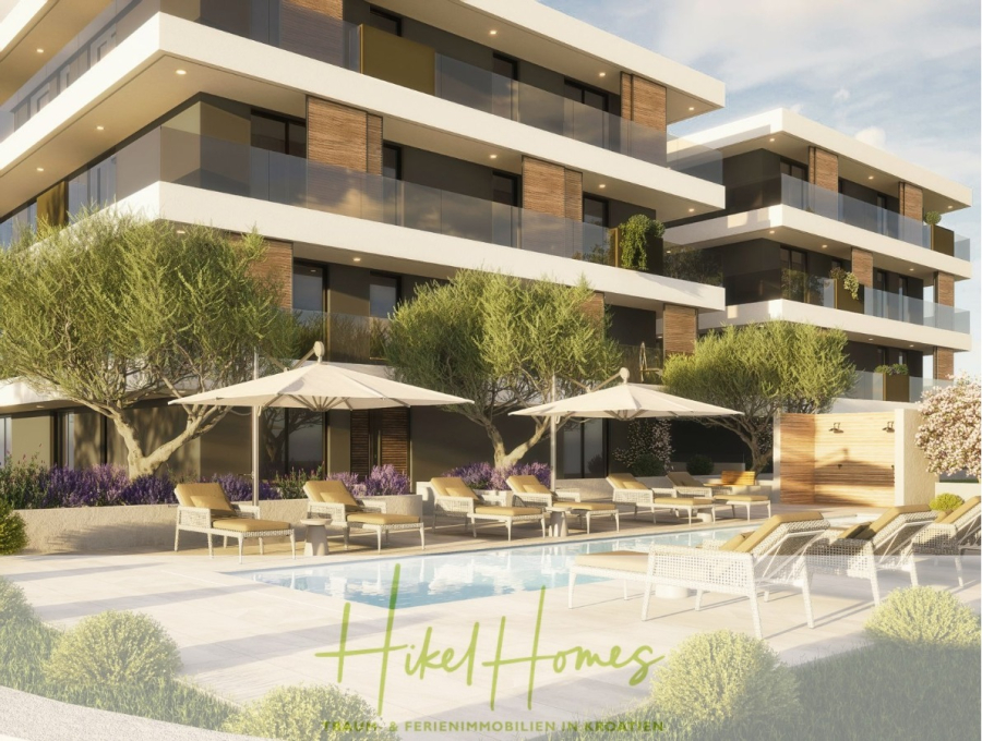 1. Reihe hochwertige Neubau-Meerblick Wohnung mit 1 SZ, Terrasse und Gemeinschaftspool (S2B) - Moderne Wohnanlage mit großen Balkonen, Liegestühlen und Sonnenschirmen am Swimmingpool, umgeben von Bäumen und angelegten Gärten unter einem sonnigen Himmel. Das Logo "Hikel Homes" ist unten sichtbar. (46163)
