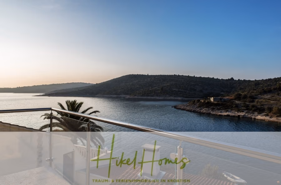 5 Sterne Villa Bruna – Meerblick auf 260m² WFL in 1. Reihe / 4 SZ / Neubau / Sofort bezugsfertig - Blick von einem Balkon auf eine ruhige, von Hügeln umgebene Bucht bei Sonnenuntergang. Im Vordergrund sind ein Geländer und eine Palme zu sehen, die Sonne wirft einen warmen Schein auf das Wasser. Der Text unten lautet: „Hikel Homes – Traum-Ferienimmobilien in Kroatien.“. (41416)