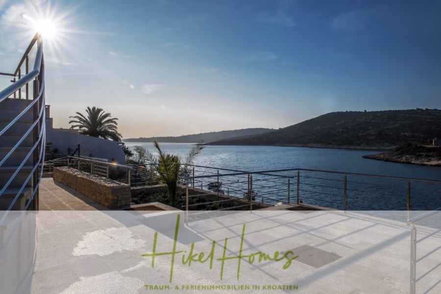 5 Sterne Villa Bruna – Meerblick auf 260m² WFL in 1. Reihe / 4 SZ / Neubau / Sofort bezugsfertig - Malerische Aussicht von einer Terrasse am Wasser auf ein ruhiges Gewässer unter sonnigem Himmel. Im Vordergrund sind ein Metallgeländer und einige Palmen zu sehen. Im Hintergrund sind sanfte Hügel über dem Wasser zu sehen. (41412)