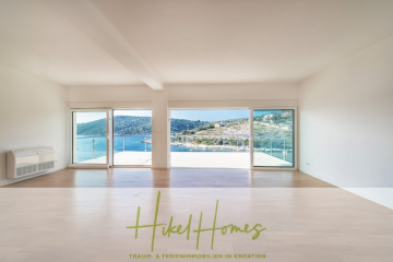 Geräumiger, leerer Raum mit großen Fenstern mit Blick auf eine malerische Küstenlandschaft mit blauem Wasser und grünen Hügeln. Der Logo-Text am unteren Rand lautet "Hikel Homes - Traum- & Ferienimmobilien in Kroatien". - 5 Sterne Villa Bruna – Meerblick auf 260m² WFL in 1. Reihe / 4 SZ / Neubau / Sofort bezugsfertig