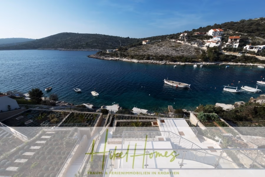 5 Sterne Villa Bruna – Meerblick auf 260m² WFL in 1. Reihe / 4 SZ / Neubau / Sofort bezugsfertig - Eine ruhige Küstenbucht mit klarem, blauem Wasser, umgeben von Hügeln und verstreuten Häusern. Boote liegen am Ufer. Im Vordergrund sind Terrassengärten und ein Hotelbanner mit dem Text „Hotel Homes“ zu sehen. (41409)