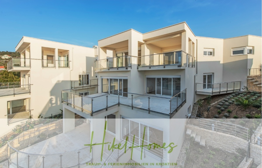 5 Sterne Villa Bruna – Meerblick auf 260m² WFL in 1. Reihe / 4 SZ / Neubau / Sofort bezugsfertig - Moderne, weiße, mehrstöckige Ferienhäuser mit großen Glasbalkonen, an einem Hang unter blauem Himmel gelegen; Textüberlagerung "Hike Homes - Traum-Ferienimmobilien in Kroatien". (46362)