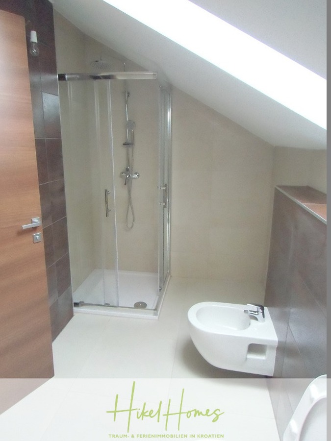 Appartement über 2 Stockwerke / 3 Schlafzimmer / 70m zum Meer / Pool / große Terrasse - Modernes Badezimmer mit schräger Decke, Glasduschabtrennung, Bidet, hellbeigen Fliesen und Holztür. Durch ein großes Oberlicht über dem Bad fällt Licht ein und schafft eine helle und saubere Atmosphäre. (46637)