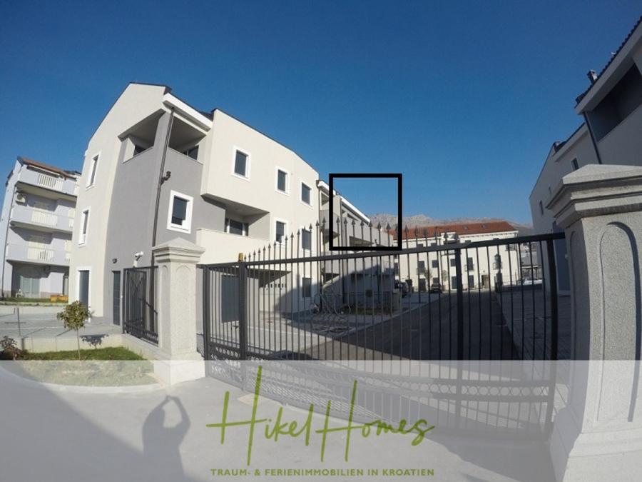 Appartement über 2 Stockwerke / 3 Schlafzimmer / 70m zum Meer / Pool / große Terrasse - Ein modernes weißes Apartmenthaus mit Balkonen ist an einem sonnigen Tag hinter einem schwarzen Metallzaun zu sehen. Das Logo von Hikel Homes und der Text "Traum- & Ferienimmobilien in Kroatien" sind am unteren Rand eingeblendet. (46643)
