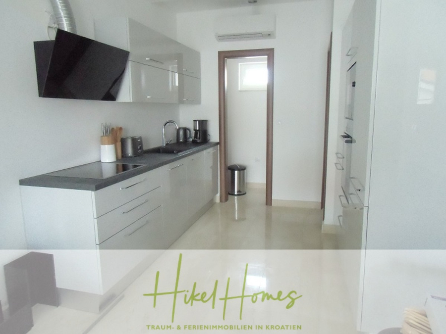 Appartement über 2 Stockwerke / 3 Schlafzimmer / 70m zum Meer / Pool / große Terrasse - Moderne, minimalistische Küche mit weißen Schränken, schwarzen Arbeitsplatten, Einbaugeräten und kleinen Küchengeräten auf der Theke. Ein Fenster und ein Mülleimer befinden sich am anderen Ende. Der Schriftzug "Hikel Homes" ist am unteren Rand eingeblendet. (46635)