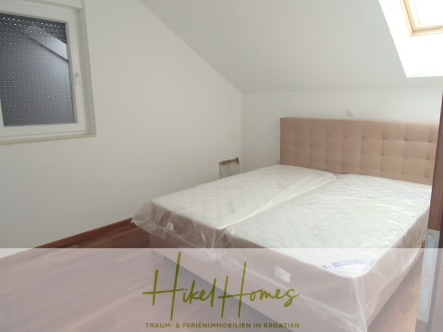 Appartement über 2 Stockwerke / 3 Schlafzimmer / 70m zum Meer / Pool / große Terrasse - Ein Schlafzimmer mit Holzboden verfügt über ein Doppelbett mit gepolstertem Kopfteil, das mit Plastik umwickelt ist. Es gibt ein einzelnes Fenster mit einem teilweise geöffneten Rollo, und ein Oberlicht erhellt den Raum. Unten ist ein Logo mit der Aufschrift „Hikel Homes“ zu sehen. (41229)