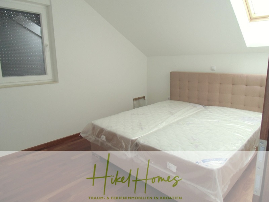 Appartement über 2 Stockwerke / 3 Schlafzimmer / 70m zum Meer / Pool / große Terrasse - Ein einfaches Schlafzimmer mit einem mit Kunststoff bezogenen Doppelbett, einem getufteten Kopfteil, Holzböden, einem Fenster mit Fensterläden und einer schrägen Decke. Das Logo "Hikel Homes" mit dem Slogan überlagert den unteren Teil des Bildes. (46639)