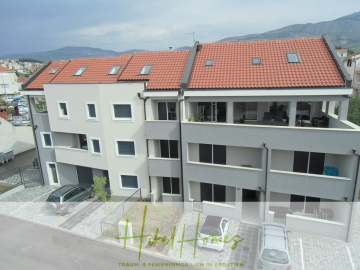 Ein modernes, dreistöckiges Wohnhaus mit rotem Ziegeldach, mehreren Balkonen und Parkplätzen davor. Das Gebäude befindet sich vor einer Bergkulisse unter klarem Himmel. - Appartement über 2 Stockwerke / 3 Schlafzimmer / 70m zum Meer / Pool / große Terrasse