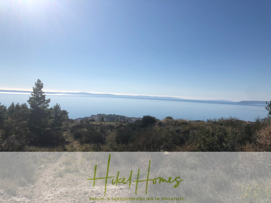 511m² Traumvilla auf über 3100m² großem unverbaubaren Meerblick Grundstück – eigene Auffahrt - Eine malerische Aussicht auf ein ruhiges blaues Meer unter einem klaren Himmel, mit Hügeln und spärlichen Bäumen im Vordergrund. Das Bild enthält ein transparentes Banner am unteren Rand mit dem Text "Hikel Homes" und weiteren Worten in deutscher Sprache. (46424)