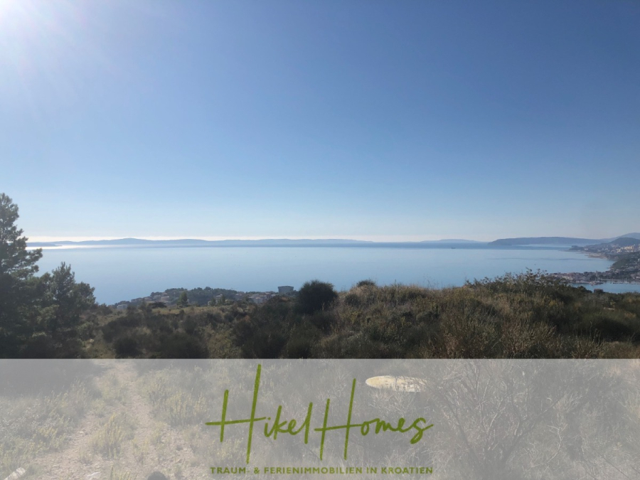 511m² Traumvilla auf über 3100m² großem unverbaubaren Meerblick Grundstück – eigene Auffahrt - Ein malerischer Blick auf die kroatische Küste mit blauem Meer, fernen Hügeln und klarem Himmel, von einem grasbewachsenen Hügel aus gesehen. Am unteren Rand befindet sich ein durchsichtiges Banner mit dem Text "Hikel Homes" und "Traum- & Ferienimmobilien in Kroatien". (46427)