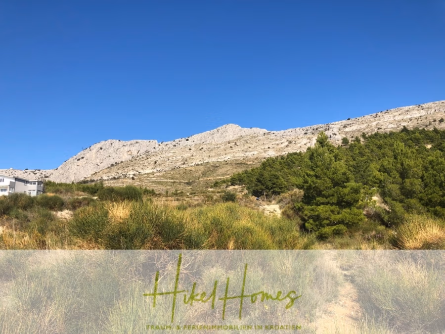 511m² Traumvilla auf über 3100m² großem unverbaubaren Meerblick Grundstück – eigene Auffahrt - Eine malerische Landschaft mit klarem, blauem Himmel über einem schroffen, felsigen Hügel mit grünen Flecken. Im Vordergrund stehen einige kleine Bäume und Büsche. Unten befindet sich ein Overlay-Text zum Thema Immobilien. (41954)