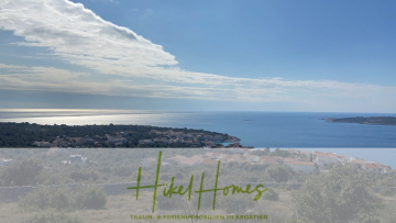 Eine malerische Küstenansicht eines Dorfes in Kroatien, mit grünen Hügeln, Häusern und dem blauen Meer unter einem teilweise bewölkten Himmel. Der Text "Hikel Homes" und "Traum- & Ferienimmobilien in Kroatien" erscheint am unteren Rand. - 805m² Bauland in Panoramahanglage mit traumhaften Rundumblick aufs Meer und die vorgelagerten Inseln