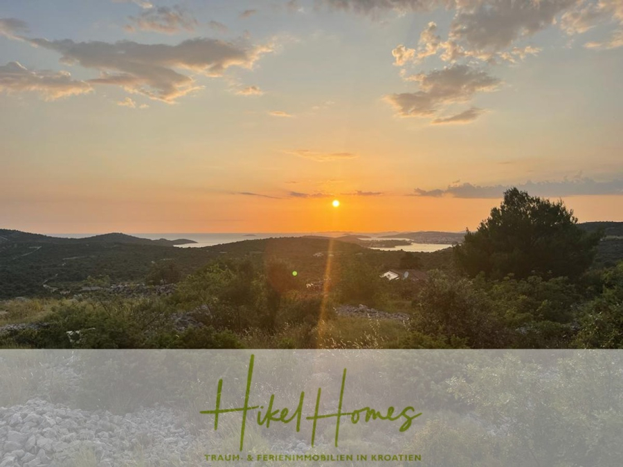 Prämiertes Architekturprojekt – Meerblick Luxus auf 490m² auf 1800m² Grund mit 2 Pools, Bar, Lounge - Ein malerischer Sonnenuntergang über einer grünen, hügeligen Landschaft mit entferntem Wasser und Inseln. Der Himmel ist teilweise bewölkt, und unten auf dem Bild steht der Text "Hikel Homes TRAUM- & FERIENIMMOBILIEN IN KROATIEN". (45076)
