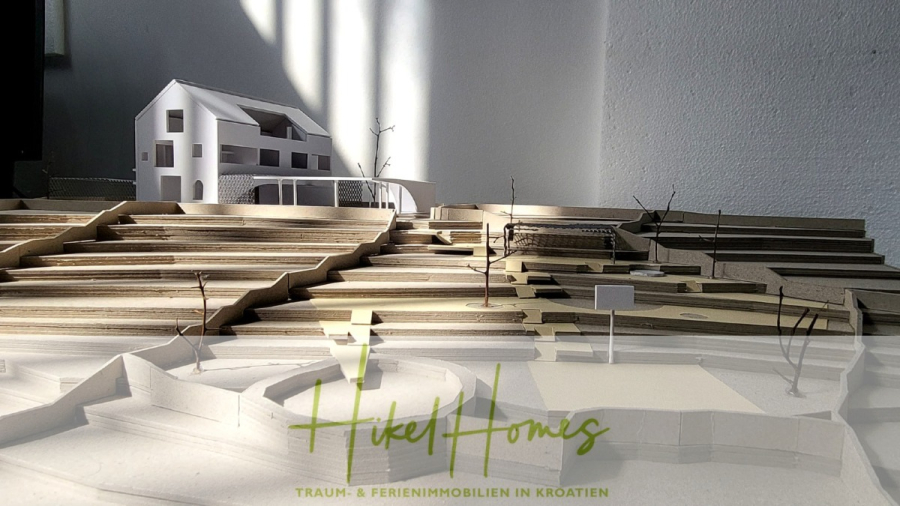 Prämiertes Architekturprojekt – Meerblick Luxus auf 490m² auf 1800m² Grund mit 2 Pools, Bar, Lounge - Ein sonnenbeschienenes Architekturmodell zeigt ein modernes weißes Haus in einer gestuften, braunen Landschaft. Kahle Modellbäume säumen das Terrain. Unten sind "Hikel Homes" und ein deutscher Text eingeblendet, der für Traumferienhäuser in Kroatien wirbt. (45071)