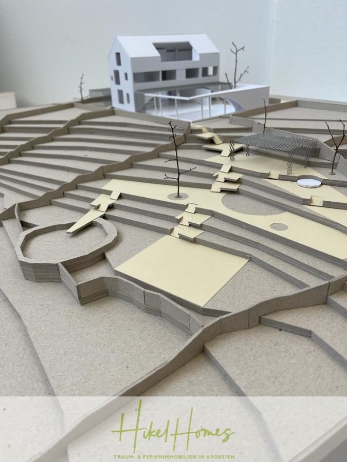 Prämiertes Architekturprojekt – Meerblick Luxus auf 490m² auf 1800m² Grund mit 2 Pools, Bar, Lounge - Ein Modell einer abgestuften Hanglandschaft mit einem modernen weißen Haus, Wegen, Terrassen, minimalistischen Bäumen und Sitzgelegenheiten, erstellt aus Karton und Papier. Das Bild trägt am unteren Rand den Schriftzug "Hiked Homes". (45072)