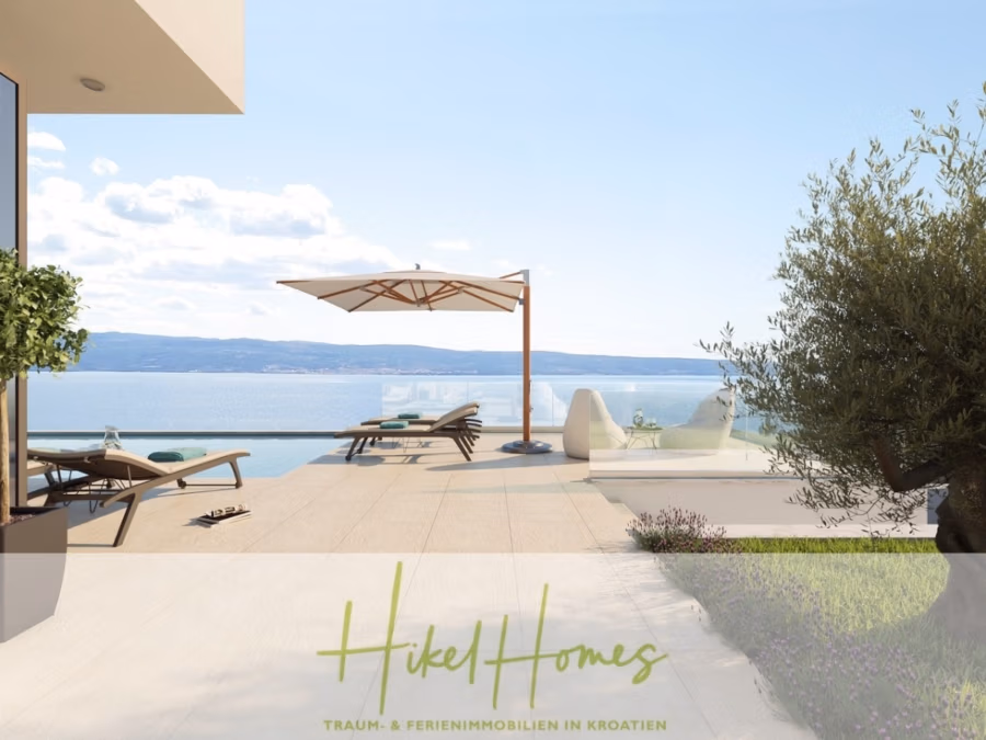 Imposante Meerblick Luxus Villa Isis – Tiefgarage, Aufzug, Wellness, Sauna, Pool, große Sommerküche - Eine moderne Terrasse mit Blick auf das ruhige, blaue Meer. Sonnenliegen und ein großer Sonnenschirm stehen auf der hellen Terrasse. Im Vordergrund steht ein Olivenbaum, am Horizont sind Hügel in der Ferne zu sehen. Die Terrasse strahlt eine ruhige, sonnige Atmosphäre aus. (42354)