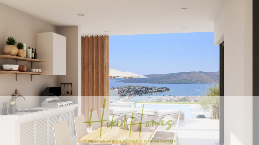 Meerblick – Schlüsselfertige Villa Princeza in Seget Vranijca – modernste Technik – 3-4 SZ - Der moderne Küchen- und Essbereich mit Holzakzenten öffnet sich zu einer Terrasse mit einem Pool und einer malerischen Aussicht auf eine Küstenstadt, Hügel und das Meer unter einem klaren Himmel. Der Text "Hikel Homes" ist überlagert. (45505)