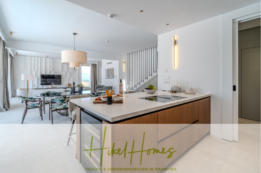 Schlüsselfertige Meerblick Villa SEA in Sutivan (Insel Brac) – 3 SZ + Bad, Pool, Sommerküche, … - Moderner offener Küchen- und Wohnbereich mit einer großen Insel, einem Esstisch mit Blumenstühlen, stilvoller Beleuchtung, einer Treppe und natürlichem Licht durch große Fenster. Branding "Hikel Homes" am Boden. (45025)