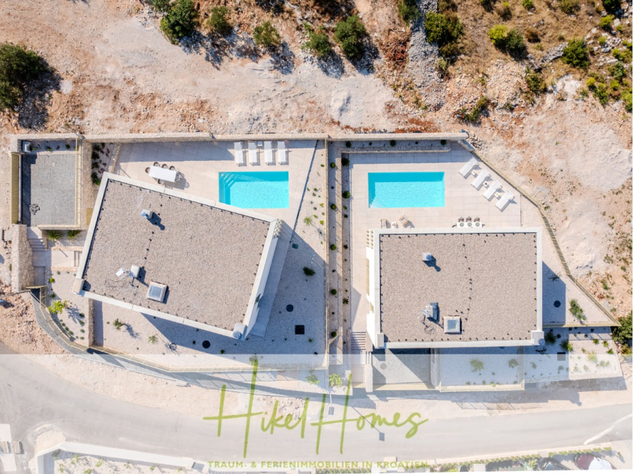 Schlüsselfertige Meerblick Villa SEA in Sutivan (Insel Brac) – 3 SZ + Bad, Pool, Sommerküche, … - Luftaufnahme von zwei modernen Villen mit privaten Pools, Liegestühlen und Terrassen, die durch einen Weg getrennt sind, umgeben von trockener, felsiger Landschaft. "Hikel Homes" und deutscher Text erscheinen am unteren Bildrand. (45012)