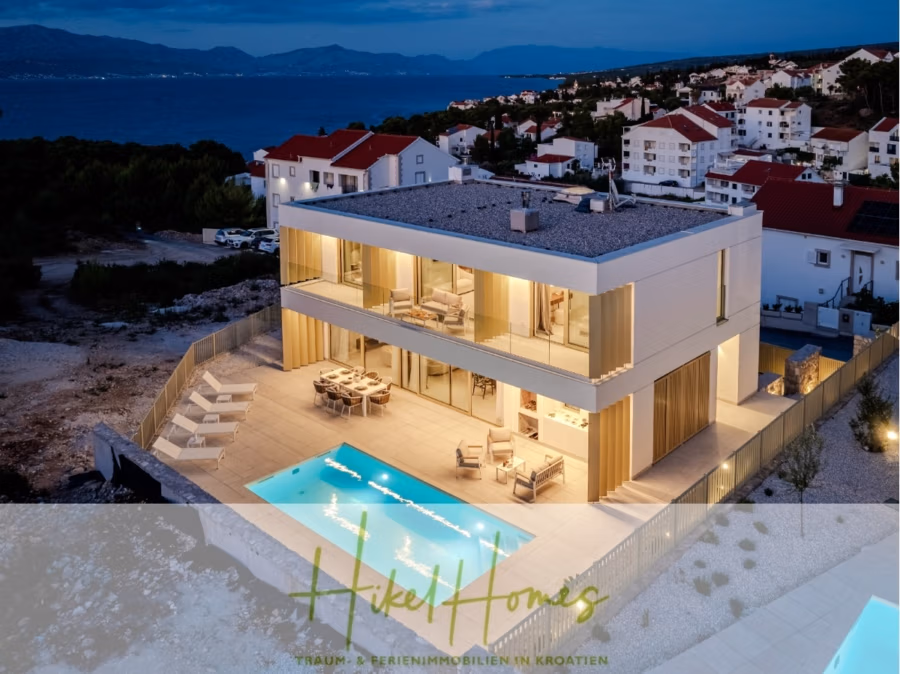Schlüsselfertige Meerblick Villa SEA in Sutivan (Insel Brac) – 3 SZ + Bad, Pool, Sommerküche, … - Eine moderne, beleuchtete zweistöckige Villa mit großen Glasfenstern und einer geräumigen Terrasse steht in der Abenddämmerung neben einem Swimmingpool. Im Hintergrund sind Häuser zu sehen und ein ruhiger Blick auf das Meer und die Berge bietet sich. (42989)