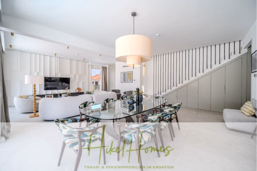 Schlüsselfertige Meerblick Villa SEA in Sutivan (Insel Brac) – 3 SZ + Bad, Pool, Sommerküche, … - Ein modernes, helles Wohnzimmer mit einem runden Esstisch und acht Stühlen. Über dem Tisch hängt eine große Pendelleuchte. Der Raum verfügt über eine Treppe, Kunstwerke an der Wand und einen Fernseher auf einem Holzschrank. Neutrale Farben sorgen für ein elegantes, luftiges Ambiente. (42995)