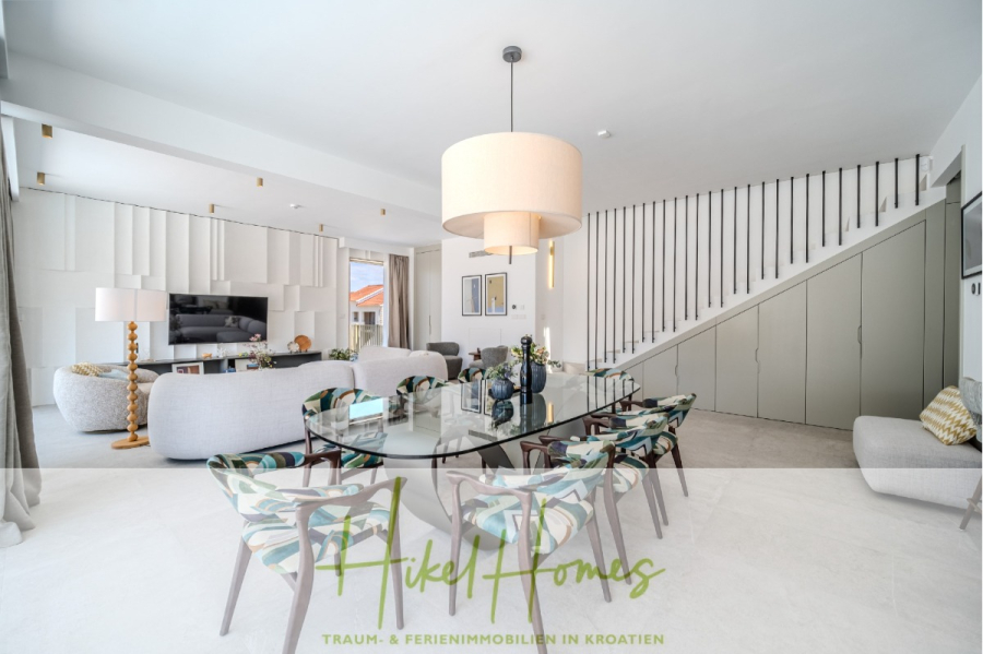 Schlüsselfertige Meerblick Villa SEA in Sutivan (Insel Brac) – 3 SZ + Bad, Pool, Sommerküche, … - Moderner, heller Wohn- und Essbereich mit einem großen Glastisch, gemusterten Stühlen, zwei Sofas, einem Fernseher und einer einzigartigen Treppe mit Stauraum darunter. Der Raum ist minimalistisch eingerichtet und verfügt über viel natürliches Licht. Das Logo "Mikel Homes" überlagert das Bild. (45020)