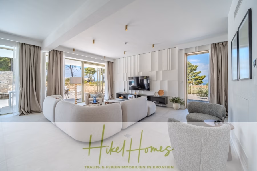 Schlüsselfertige Meerblick Villa SEA in Sutivan (Insel Brac) – 3 SZ + Bad, Pool, Sommerküche, … - Modernes Wohnzimmer mit großen Fenstern, hellen Sofas, einem Wandfernseher und zeitgenössischer Einrichtung. Der Raum bietet einen malerischen Blick auf die Natur, darunter Bäume und einen Blick auf das Meer. Der Markentext „Hikel Homes“ ist unten eingeblendet. (42997)