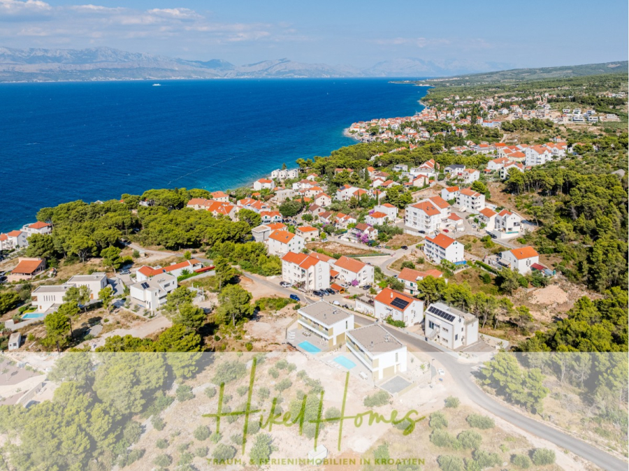 Schlüsselfertige Meerblick Villa SEA in Sutivan (Insel Brac) – 3 SZ + Bad, Pool, Sommerküche, … - Luftaufnahme einer Küstenstadt in Kroatien mit weißen Häusern und roten Dächern, umgeben von Grün und mit Blick auf das blaue Adriatische Meer. Der Text am unteren Rand lautet "Hiked Homes - Traumferienimmobilien in Kroatien. (45009)