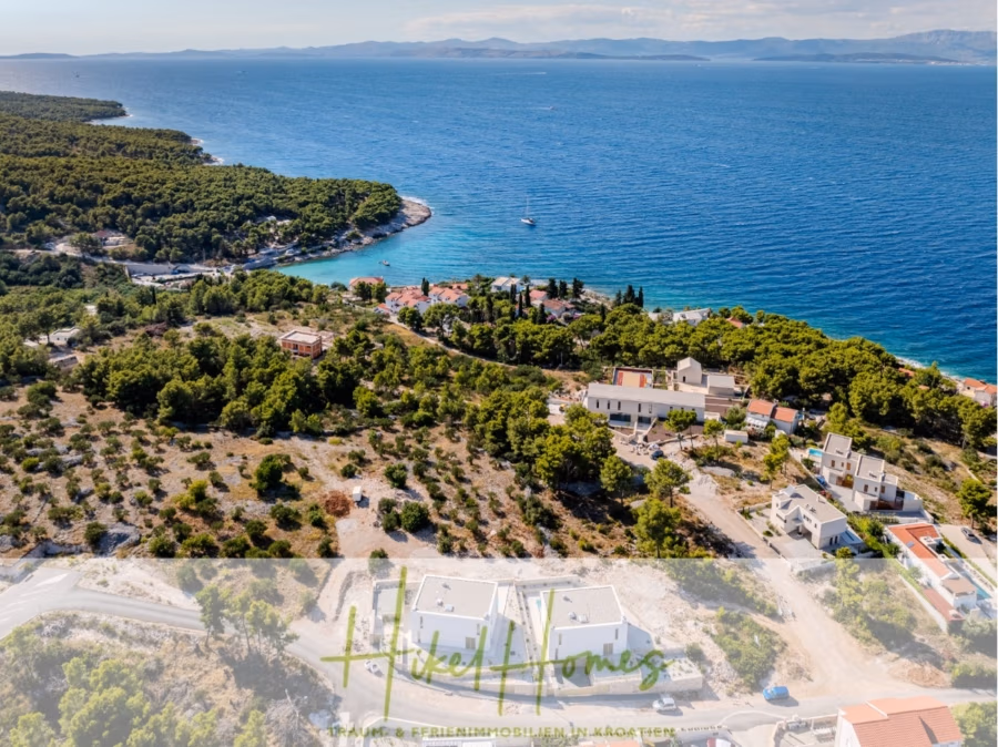 Schlüsselfertige Meerblick Villa SEA in Sutivan (Insel Brac) – 3 SZ + Bad, Pool, Sommerküche, … - Eine Luftaufnahme der Küste zeigt ein Waldgebiet, das zum klaren, blauen Meer führt. In Ufernähe sind mehrere Häuser zu sehen, im Vordergrund eine kurvenreiche Straße. Am Horizont sind fernes Land und vereinzelte Wolken zu sehen. (42986)