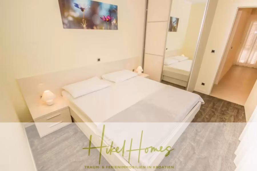 Villa im Mittelmeerstil mit 3 SZ, Pool, Dachterrasse mit Meerblick (2) - Ein ordentlich eingerichtetes Schlafzimmer mit einem Doppelbett, weißer Bettwäsche und zwei Nachttischen mit Lampen. Über dem Bett hängt ein farbenfrohes Blumenbild. Auf der einen Seite befindet sich ein Spiegelschrank, und eine Tür führt in einen beleuchteten Flur. (41884)