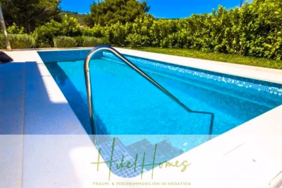 Villa im Mittelmeerstil mit 3 SZ, Pool, Dachterrasse mit Meerblick (2) - Ein heller Außenpool mit klarem, blauem Wasser und Metallgeländern, umgeben von üppigen grünen Büschen und Bäumen. Im Vordergrund sind ein Logo und der Text „Hikel Homes“ und „TRAUM- & FERIENIMMOBILIEN IN KROATIEN“ zu sehen. (41873)